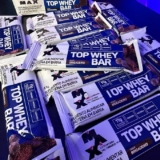 OIA O LANCHIN PRA TU NÃO SAIR DA DIETINHA Max Titanium Top Whey Bar – 12 Unidade…